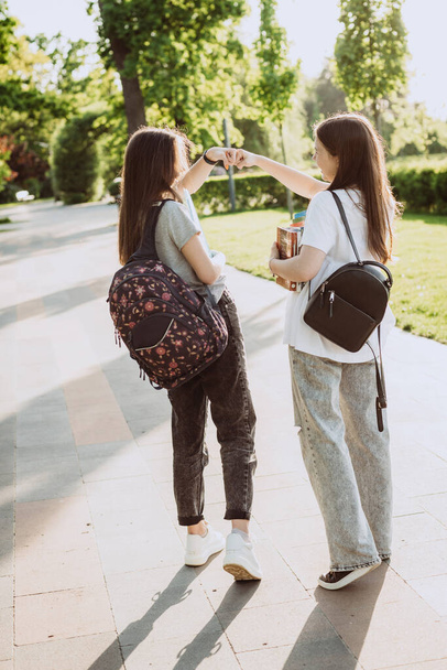 2人の女子学生は、キャンパスで会うときにお互いに挨拶をします。距離学習。柔らかい選択的フォーカス. - 写真・画像