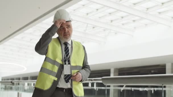 Medium POV valkoihoinen työnjohtaja yllään muodollinen vaatteet heijastava liivi, laittaa kypärä, poseeraa kädet ristissä rinnassa kameran edessä - Materiaali, video