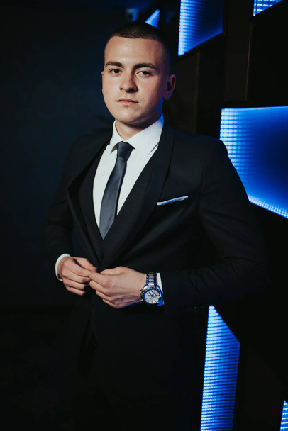 A vertical shot of a young caucasian male club manager posing in front of an illuminated wall - Photo, Image