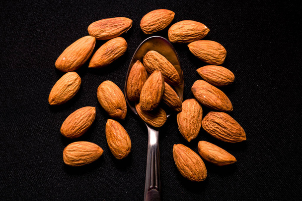 A top view of a spoon of almonds on a black background - Photo, Image
