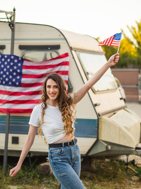 A vertical shot of a blonde Caucasian female posing with the US flag - 写真・画像