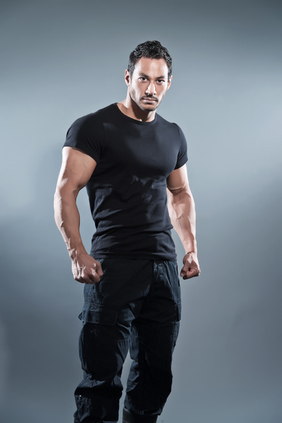 Combat muscled fitness man wearing black shirt and pants. Studio - Photo, Image