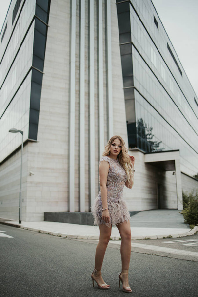 A vertical shot of a young stylish female in a cocktail dress outdoors against a modern building - Foto, immagini
