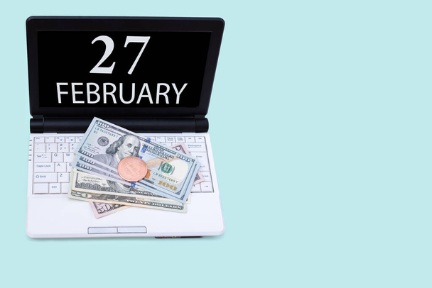 27th day of february. Laptop with the date of 27 february and cryptocurrency Bitcoin, dollars on a blue background. Buy or sell cryptocurrency. Stock market concept. Winter month, day of the year - Fotó, kép