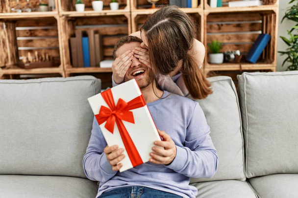 jonge vrouw verrassen haar vriend met verjaardag cadeau thuis. - Foto, afbeelding