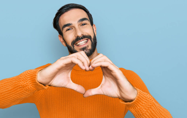 Jonge Latijns-Amerikaanse man draagt casual kleding glimlachend in de liefde doen hart symbool vorm met de handen. romantisch concept.  - Foto, afbeelding