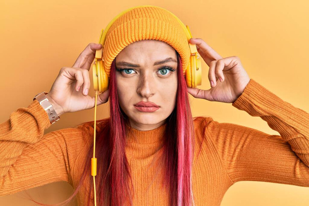 Νεαρή καυκάσια γυναίκα που ακούει μουσική χρησιμοποιώντας ακουστικά σκεπτικιστική και νευρική, συνοφρυωμένη λόγω προβλήματος. αρνητικό πρόσωπο.  - Φωτογραφία, εικόνα