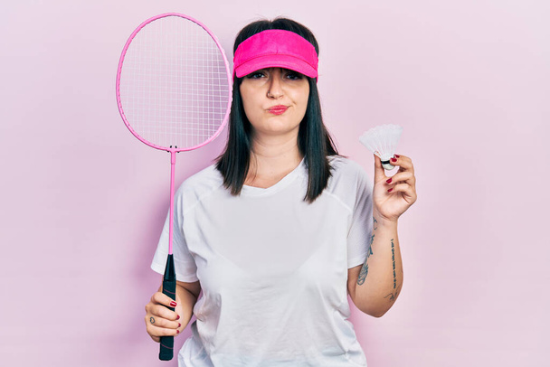 Junge hispanische Frau mit Badmintonschläger und Federball skeptisch und nervös und runzelt die Stirn wegen des Problems. negative person.  - Foto, Bild