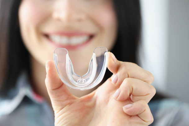 glimlachende vrouw houdt transparante plastic mondbeschermer in haar hand - Foto, afbeelding