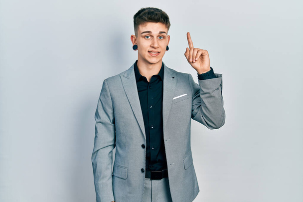 Young caucasian boy with ears dilation wearing business jacket showing and pointing up with finger number one while smiling confident and happy.  - Photo, Image