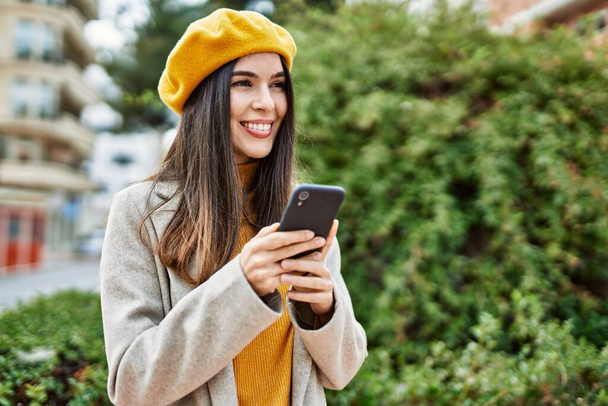 Junges hispanisches Mädchen lächelt glücklich mit Smartphone in die Stadt. - Foto, Bild
