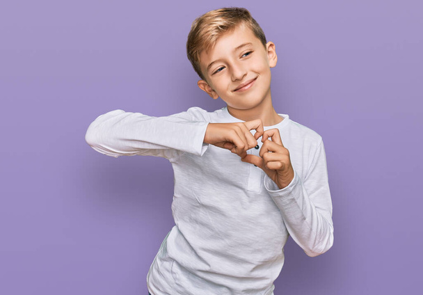 Petit garçon caucasien enfant portant des vêtements décontractés souriant en amour faisant forme de symbole de coeur avec les mains. concept romantique.  - Photo, image