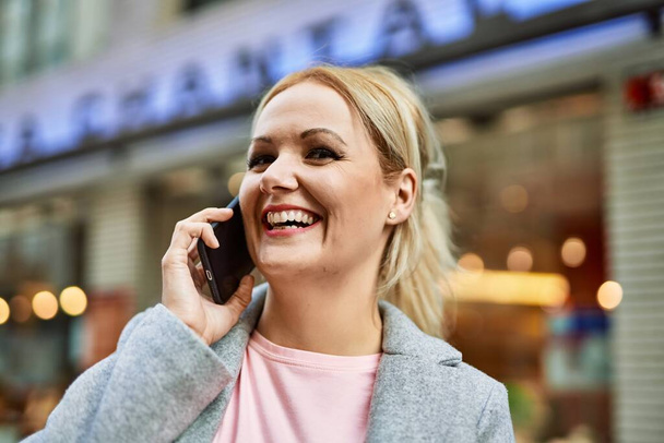 Young blonde businesswoman smiling happy talking on the smartphone at the city. - Фото, изображение