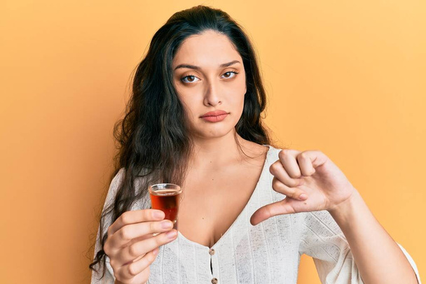 Ortadoğulu güzel bir kadın kızgın suratlı viski içiyor, olumsuz işaret baş parmakları aşağıda, reddedilme konsepti reddedildi.  - Fotoğraf, Görsel