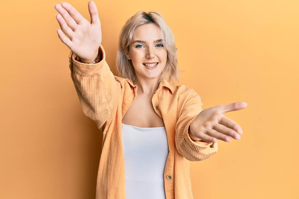 Young blonde girl wearing casual clothes looking at the camera smiling with open arms for hug. cheerful expression embracing happiness.  - Fotoğraf, Görsel