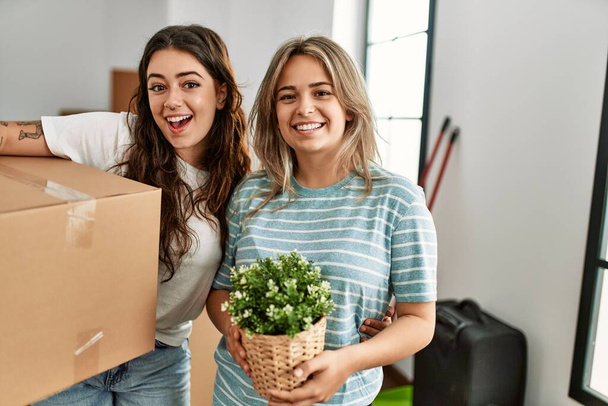 Young beautiful couple smiling happy holding cardboard box and plant pot at new home. - Photo, Image