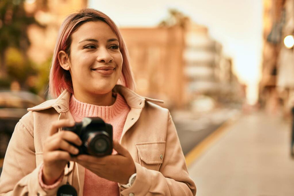 Giovane ragazza ispanica sorridente felice con fotocamera reflex in città. - Foto, immagini