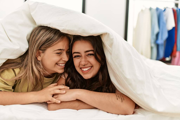 Jeune couple souriant heureux couvrant avec drap couché sur le lit. - Photo, image