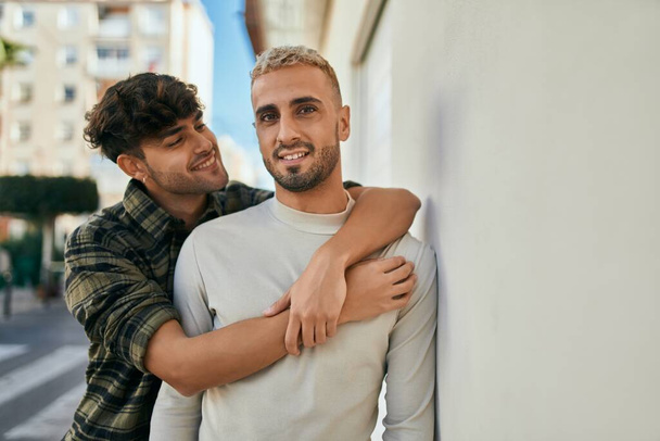 Joven pareja gay sonriendo feliz y abrazando en la ciudad. - Foto, imagen
