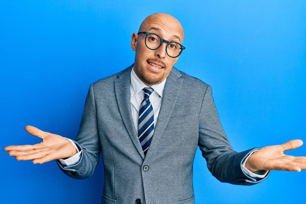 Bald man with beard wearing business jacket and glasses clueless and confused expression with arms and hands raised. doubt concept.  - Photo, Image