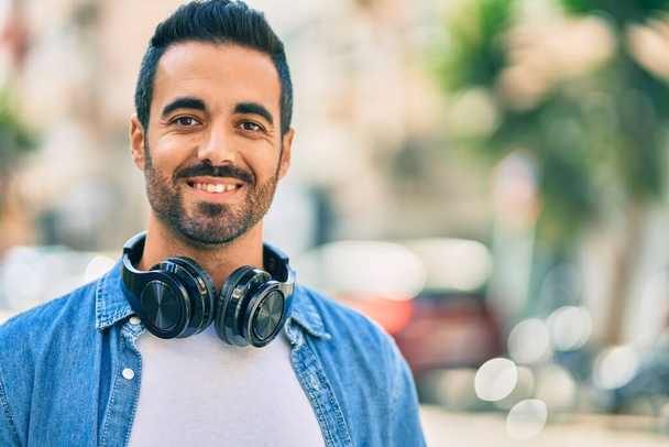 Jovem hispânico sorrindo feliz usando fones de ouvido na cidade. - Foto, Imagem