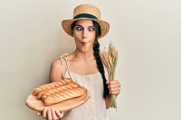 Nuori latino nainen tilalla kotitekoinen leipää ja piikki vehnä tehdä kala kasvot suulla ja siristää silmät, hullu ja koominen.  - Valokuva, kuva