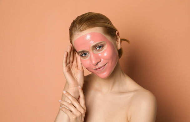 Young woman with pomegranate face mask on pale coral background - Фото, изображение