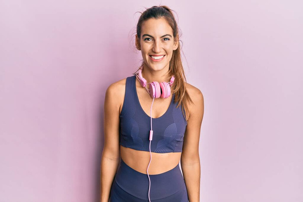 Young beautiful woman wearing gym clothes and using headphones with a happy and cool smile on face. lucky person.  - Photo, Image