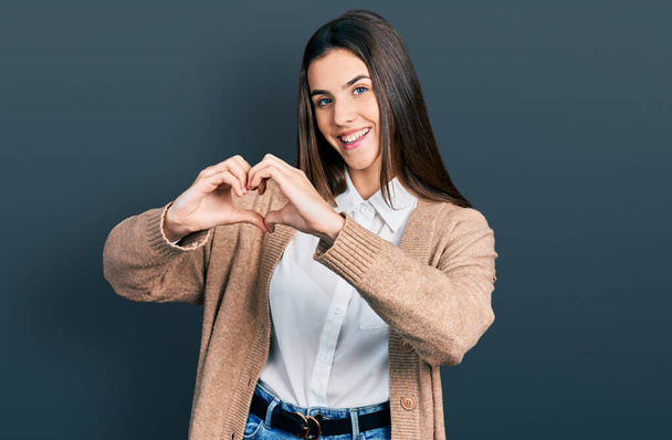 Mladá brunetka teenager nosit ležérní bílou košili a bundu s úsměvem v lásce ukazující symbol srdce a tvar s rukama. romantický koncept.  - Fotografie, Obrázek