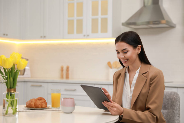 Young woman with tablet having breakfast in kitchen. Morning routine - Photo, image
