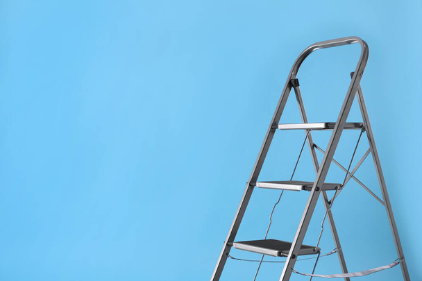 Metal stepladder on light blue background, space for text. Construction equipment - Foto, afbeelding