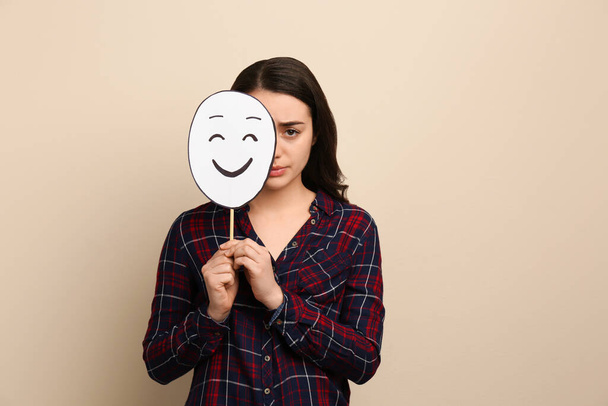 Sad woman hiding behind happy paper face on beige background - Photo, image