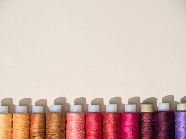 Sewing thread spools. View from above. Beautiful multi-colored spools of thread lying in a row on a pale yellow background. Bright threads. The shadow from the coils. A beautiful set for a seamstress without a needle. Copy space. - Foto, Imagem