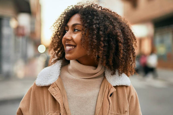 Młoda afrykańska kobieta uśmiecha się szczęśliwa stojąc w mieście. - Zdjęcie, obraz