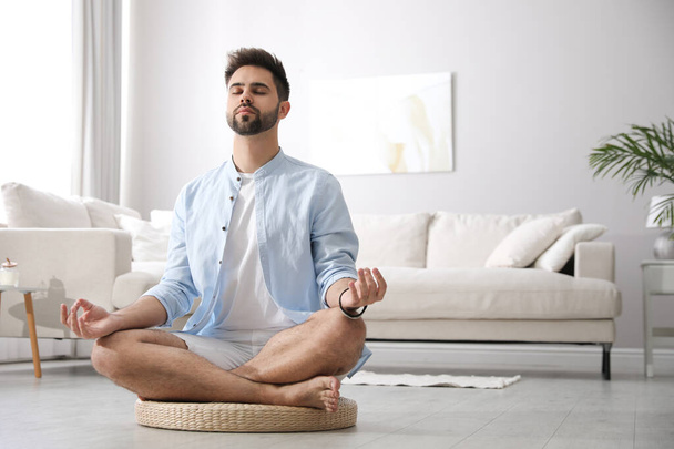Young man meditating on straw cushion at home, space for text - Foto, Imagen