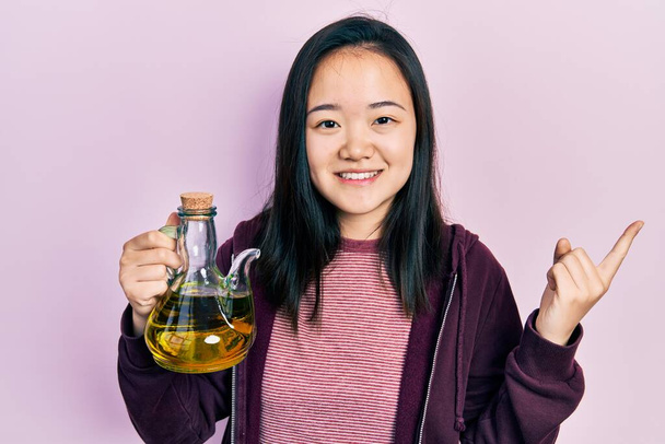 Young chinese girl holding olive oil can smiling happy pointing with hand and finger to the side  - Φωτογραφία, εικόνα