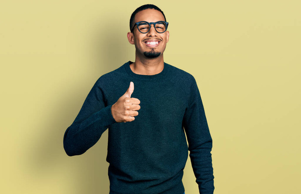 Jonge Afro-Amerikaanse man met casual kleding en een bril die met de hand een gebaar maakt. goedkeuring van expressie kijken naar de camera toont succes.  - Foto, afbeelding