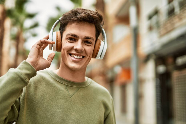 Jonge Spaanse man lacht gelukkig met behulp van koptelefoon in de stad. - Foto, afbeelding