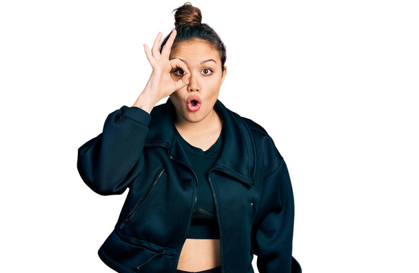 Young hispanic girl wearing sportswear doing ok gesture shocked with surprised face, eye looking through fingers. unbelieving expression.  - Photo, Image