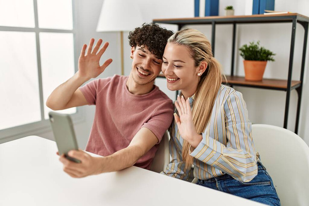 Jovem casal sorrindo feliz fazendo chamada de vídeo usando smartphone em casa. - Foto, Imagem