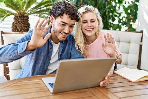 Fiatal pár mosolyog boldog, hogy videohívás segítségével laptop ül az asztalon a teraszon. - Fotó, kép