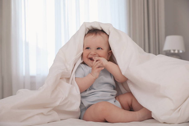 Cute little baby under soft blanket on bed at home - Fotó, kép