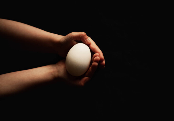 Kinderhände halten ein Ei auf dunklem Hintergrund - Foto, Bild