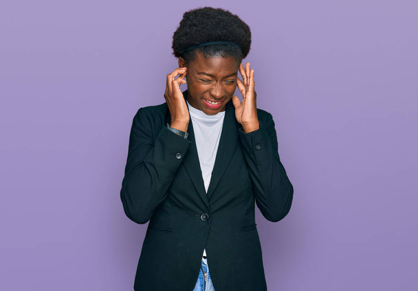 Jovem afro-americana vestindo roupas de negócios cobrindo orelhas com dedos com expressão irritada para o ruído da música alta. conceito surdo.  - Foto, Imagem