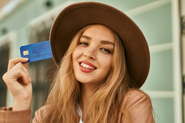 Young blonde girl smiling happy holding credit card at the city. - 写真・画像