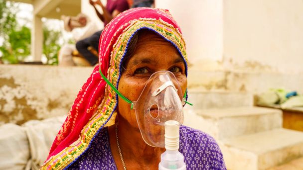 old woman infected with Covid 19 disease. Patient inhaling oxygen wearing mask with liquid Oxygen flow. - 写真・画像