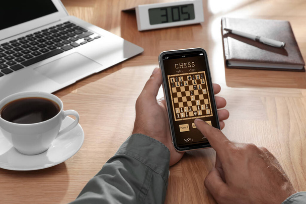 Man playing online chess on smartphone at table, closeup - Fotoğraf, Görsel