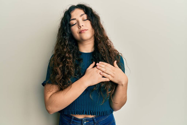 Young brunette woman with curly hair wearing casual clothes smiling with hands on chest with closed eyes and grateful gesture on face. health concept.  - Photo, Image