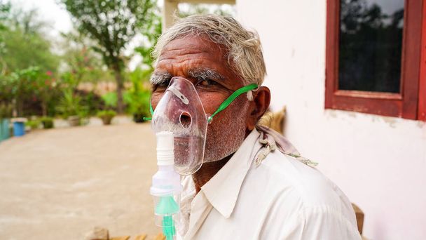 Ein älterer Mensch, der mit Covid 19 infiziert ist. Patient inhaliert Sauerstoffmaske mit flüssigem Sauerstofffluss. - Foto, Bild