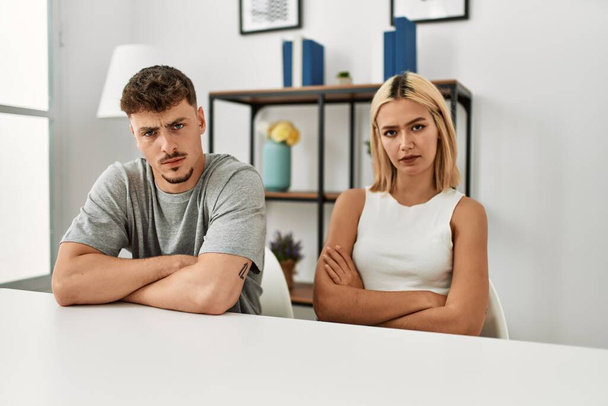 Young beautiful couple wearing casual clothes sitting on the table at home skeptic and nervous, disapproving expression on face with crossed arms. negative person.  - Φωτογραφία, εικόνα